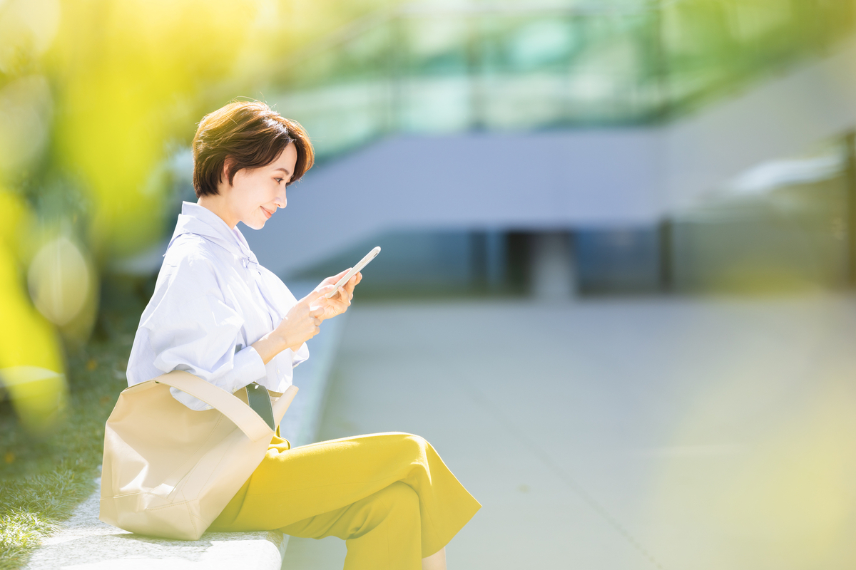 屋外で座ってスマホを触る女性