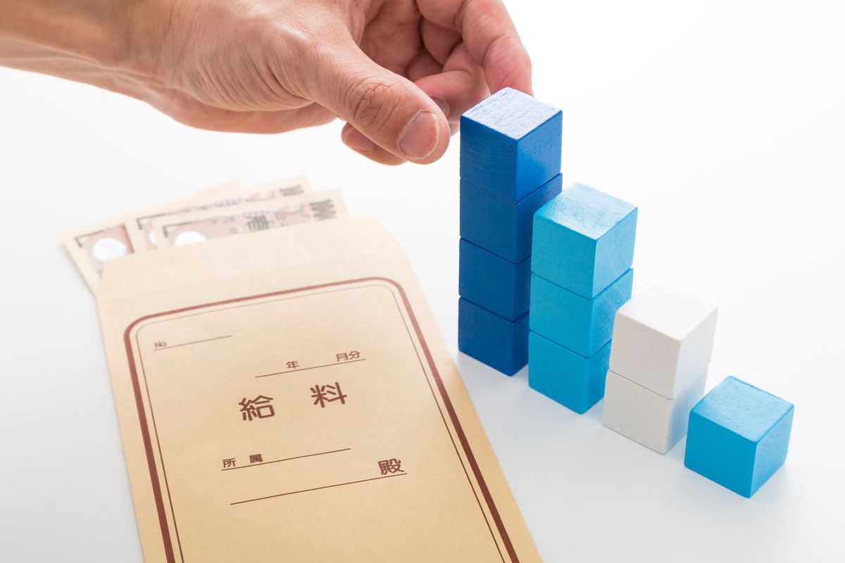 給与とブロックを階段状に積み上げる男性の手