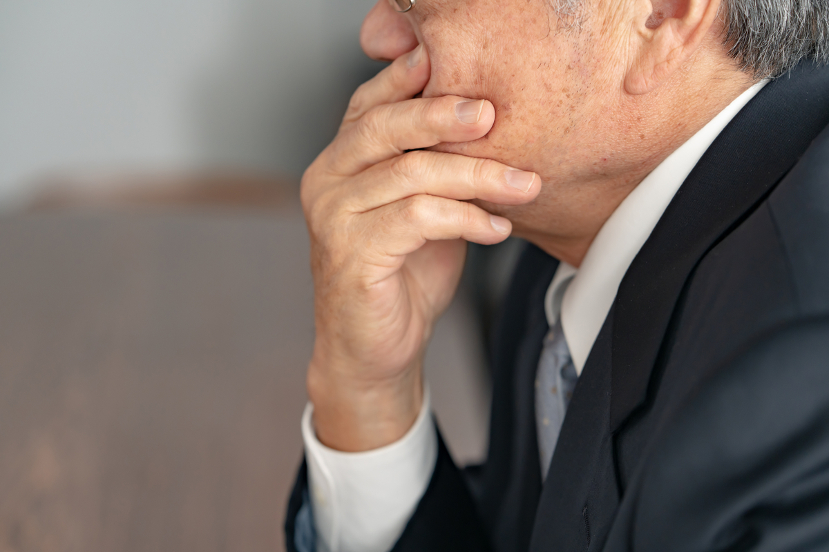 口元を手で覆うシニア男性