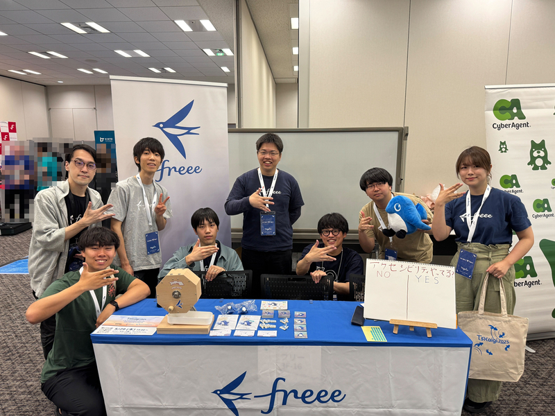 freeeのスポンサーブースで参加メンバーが右手をパーの状態から人差し指と中指、薬指と小指をくっつけたフリーのアイコンを表すポーズをしている