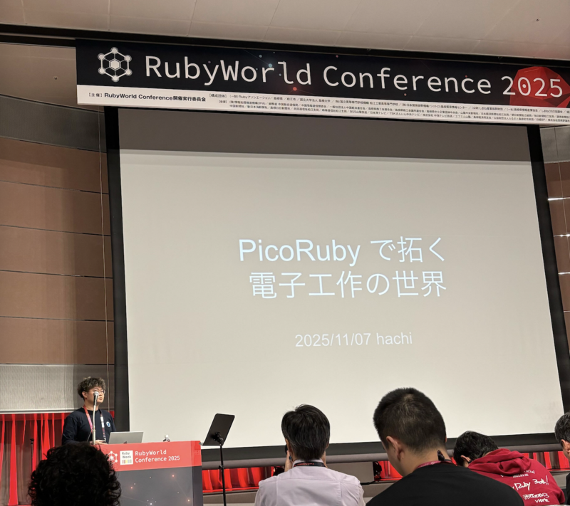 はっちさんが壇上で話しており、「PicoRuby で拓く電子工作の世界」という書いてあるスライドが写っている