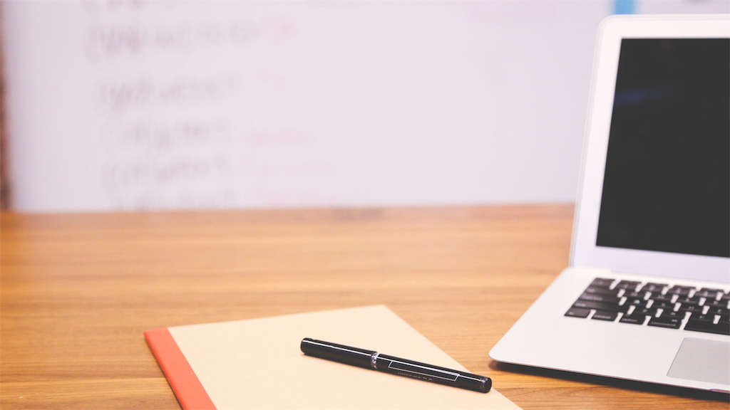 机の上にノートパソコンとペンとノートが置いてある