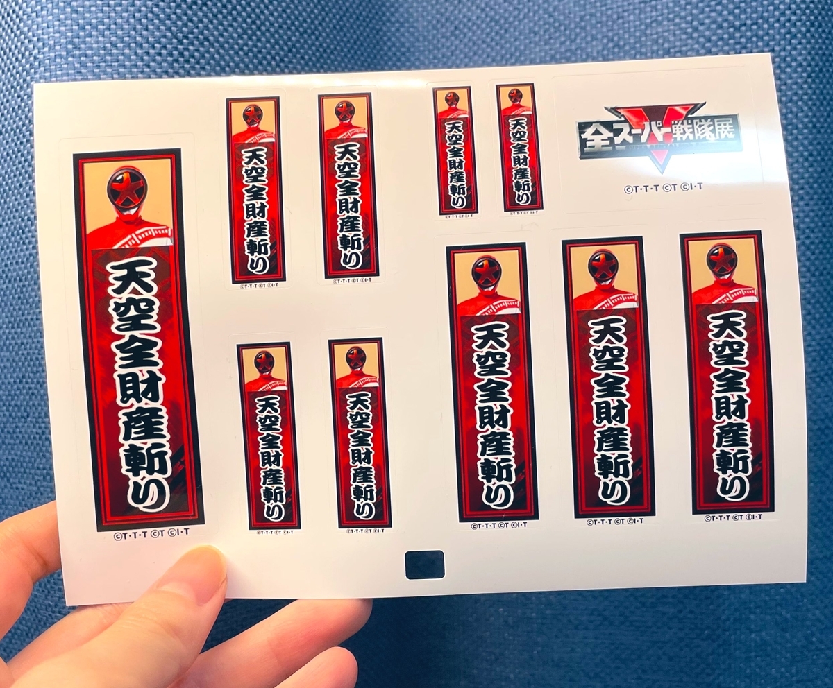 「天空全財産斬り」とプリントされたシールを持っている