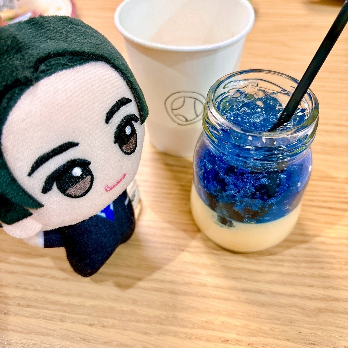 ビンに入ったプリン（上に青いゼリーが乗っている）と、その横にシャーシロのぬいぐるみ。後ろには下手なブンブルーの書かれた紙コップが映り込んでいる