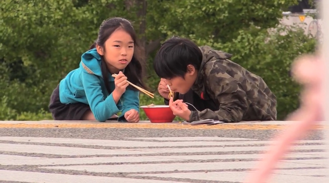 地べたに寝転んでタイヘンにお行儀よくラーメンを食す子どもたち。