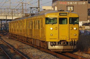 直線区間を走り中庄駅に入線する115系(D-21編成)。黄色い電車