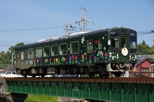 二俣川橋梁(緑色のガーター橋)を渡る天竜浜名湖鉄道TH2100形(TH2107・花のリレー・プロジェクトラッピング列車)。深緑色のラッピング列車