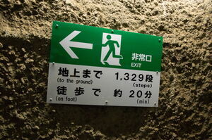 「地上まで1329段」「徒歩で約20分」と書かれた非常口案内看板