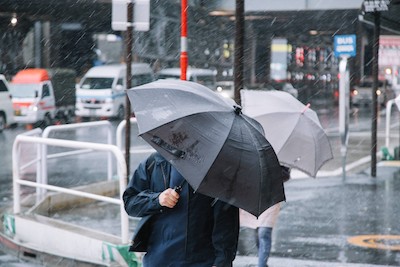 前が見えないほどの雨の中、傘をさし歩いている会社員