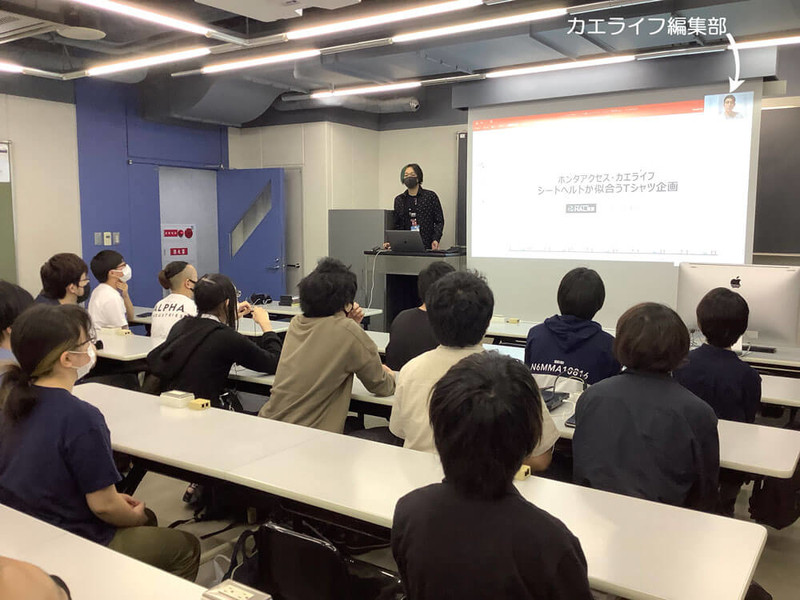 専門学校HALのある教室内でカエライフの企画「シートベルトが似合うTシャツ企画」の説明動画を流している写真