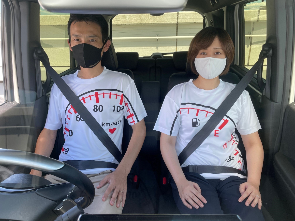 シートベルトが似合うTシャツコンテスト【カエライフ最優秀賞】の実物のTシャツを着て、運転席・助手席に座っている写真