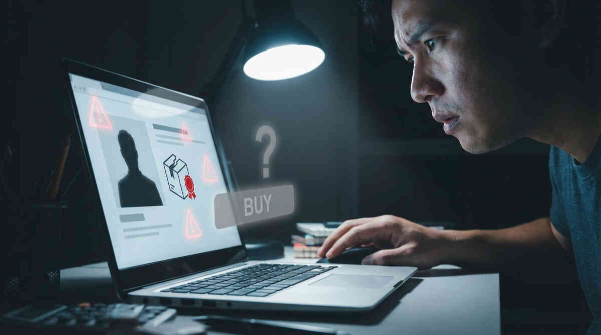 Serious man leaning toward his laptop in a dark room, face lit by warning triangles and a cracked box icon on a suspicious product page with a ghosted BUY button and question mark—tense decision moment about risky third-party Apple sellers on Amazon, alert and cautious vibe