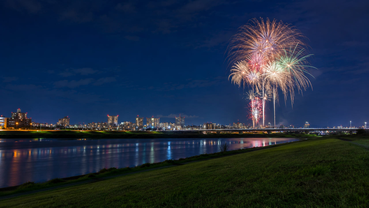 川越しに遠くの花火を眺める河川敷の夜景