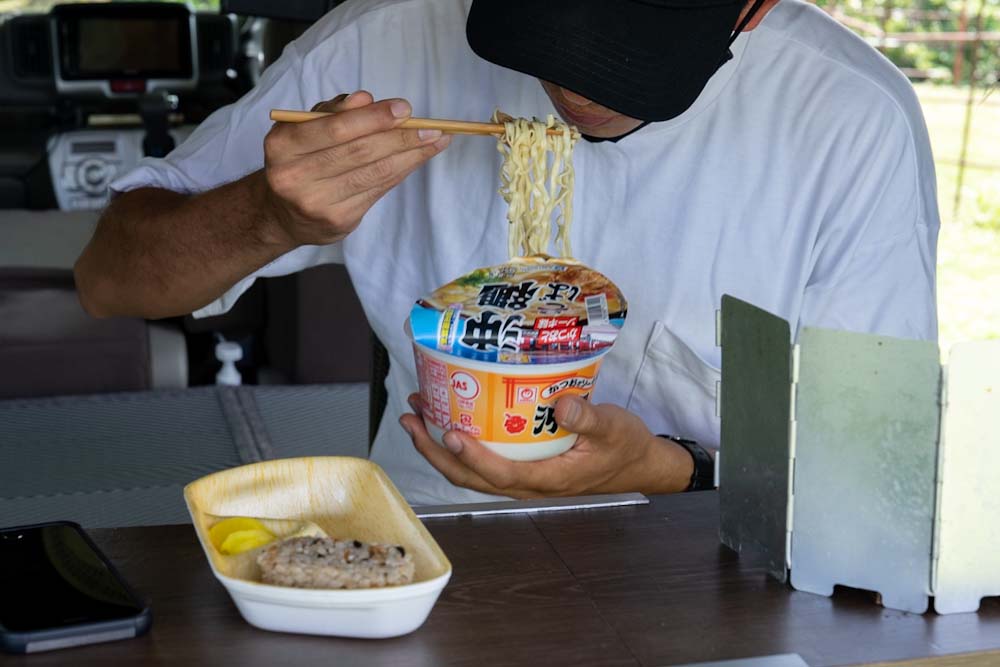 カップ麺の沖縄そばとジューシーおにぎりを、車内で食べるカメコロー氏