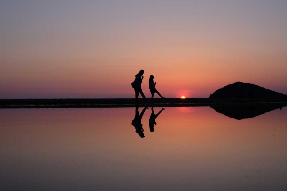 父母ヶ浜の特徴を捉えた夕日と人物が陽だまりに映り込んだ１枚