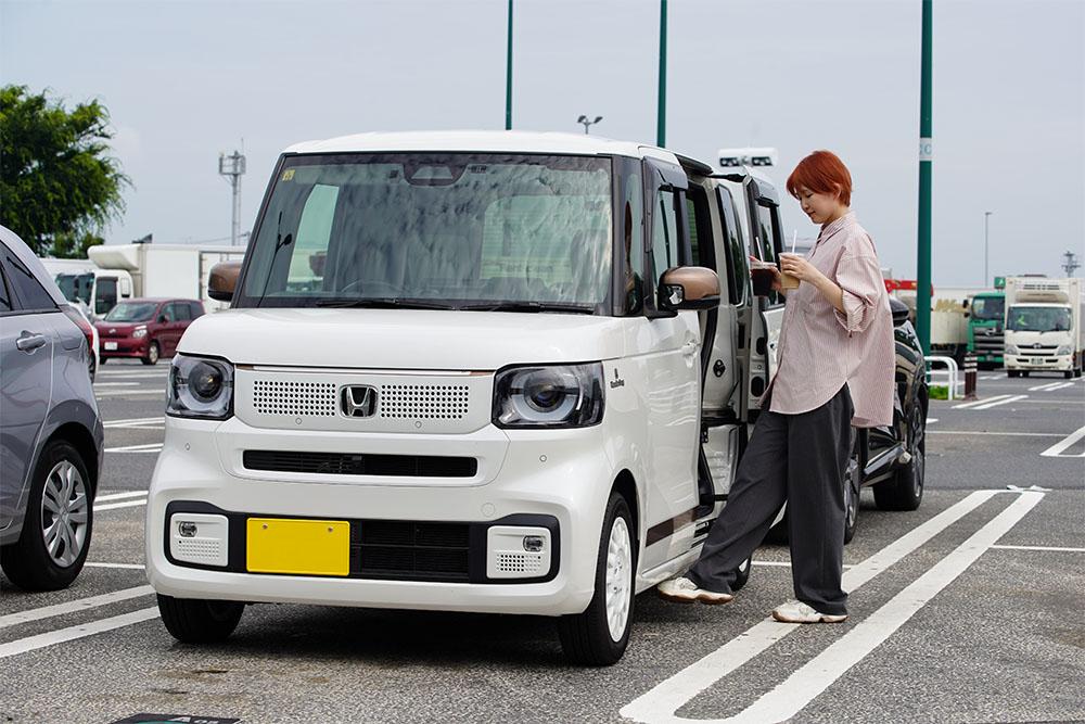 両手にドリンクを持っている女性が、N-BOX用純正アクセサリーハンズフリースライドドアを使っている様子