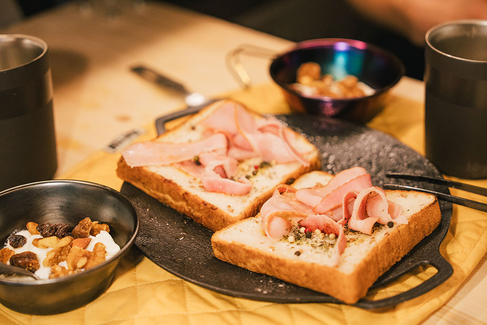 ベーコンを乗せバジルを振りかけたライ麦パンに、ナッツ&レーズンをかけたヨーグルトにコーヒー