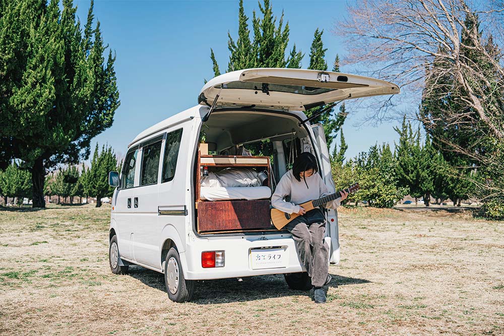 開けたバックドアに腰かけ、ギターを弾くいとうさん