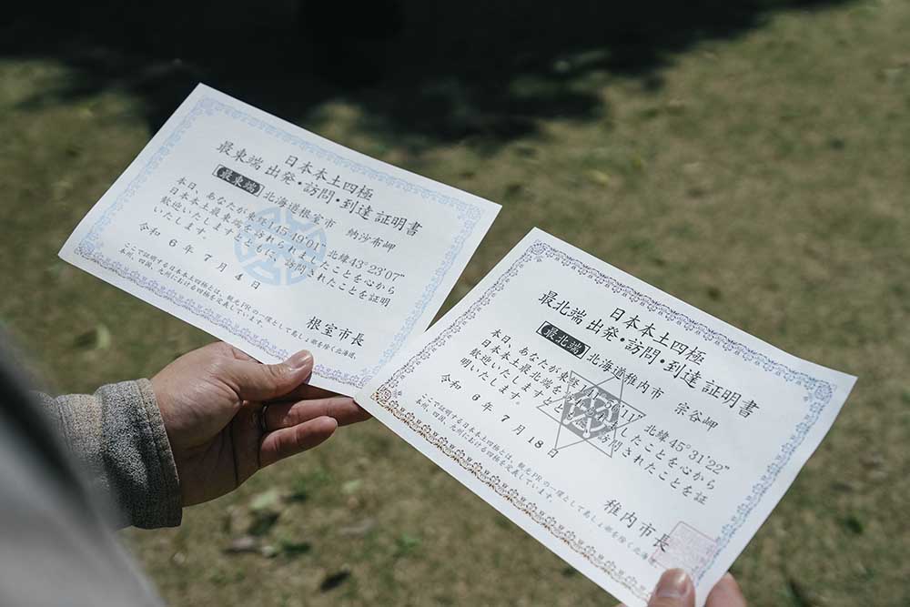 日本一周途中にもらった「日本本土四極踏破証明書」の内の２枚を持っている様子