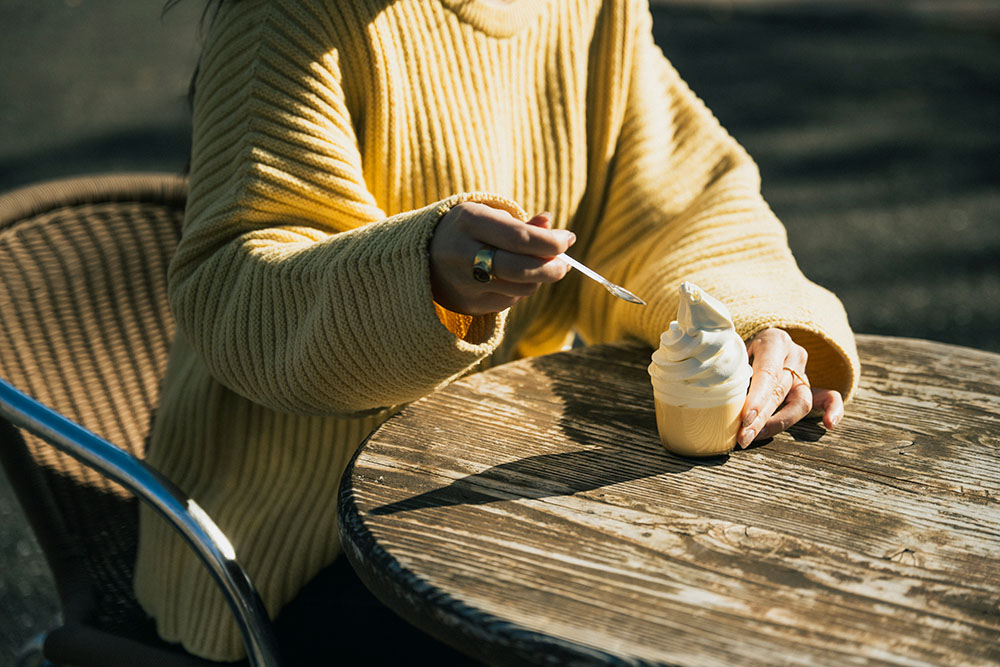 レストハウスやまなみのプリンソフトをテラス席で食べる女性