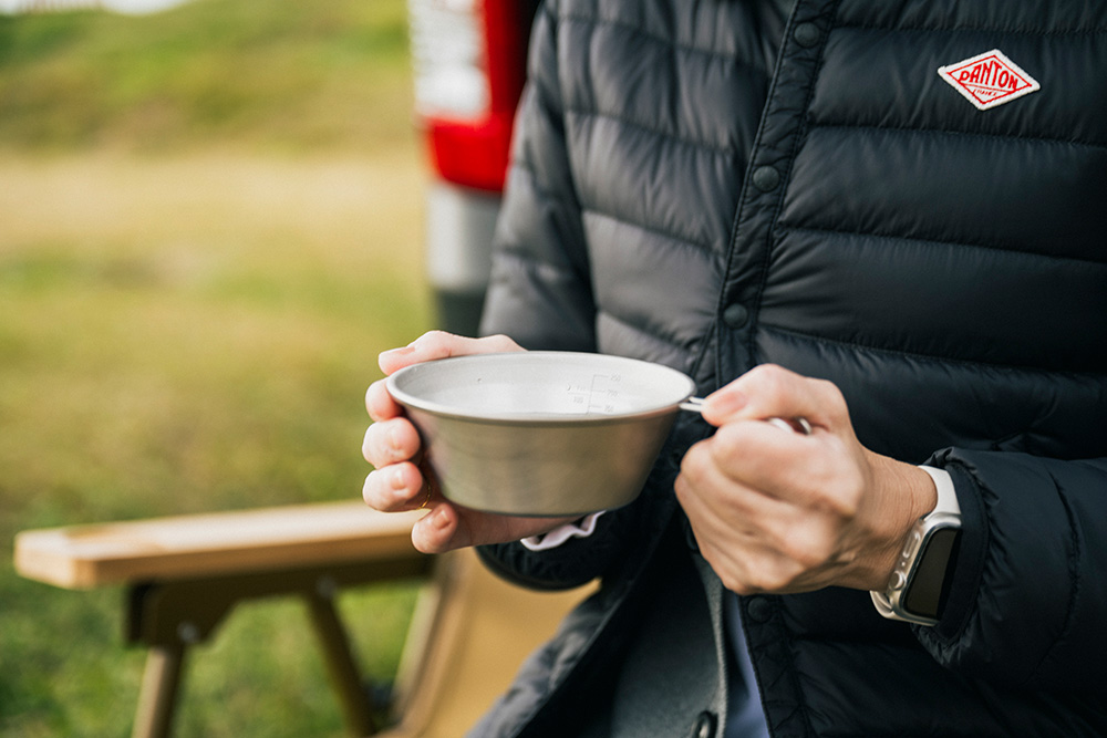 外で入れたコーヒーのカップを手に持つ女性