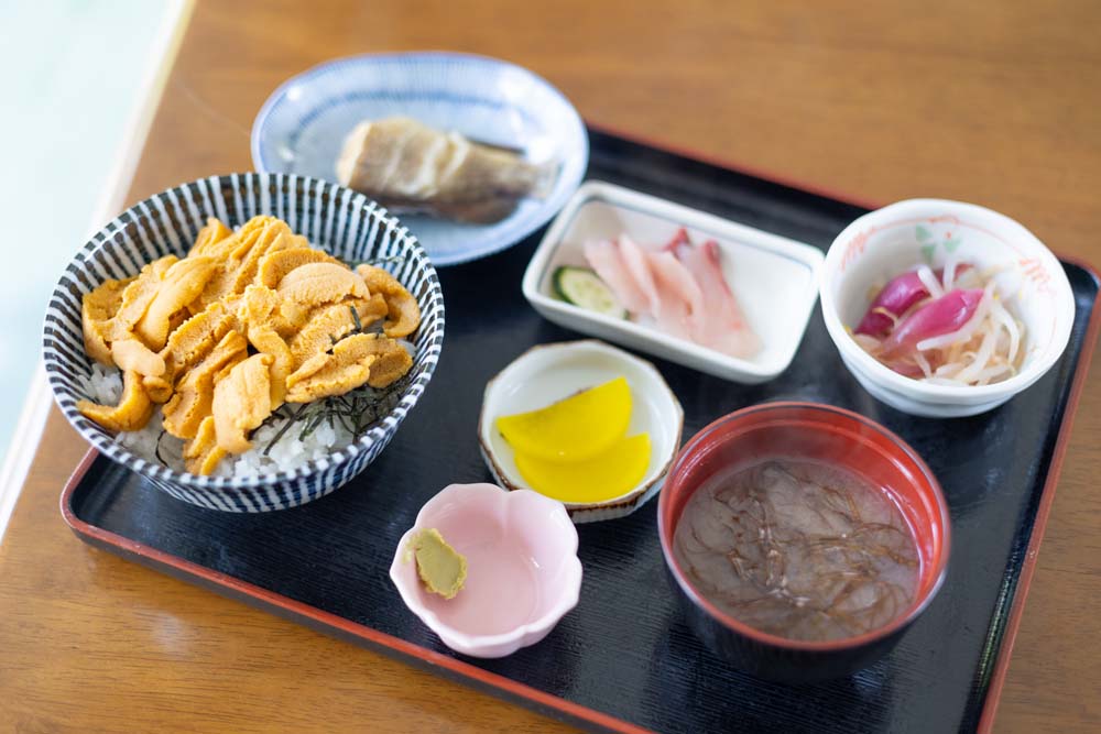 ウニ丼に刺身、メバルの煮つけ、漬物やみそ汁が並ぶ
