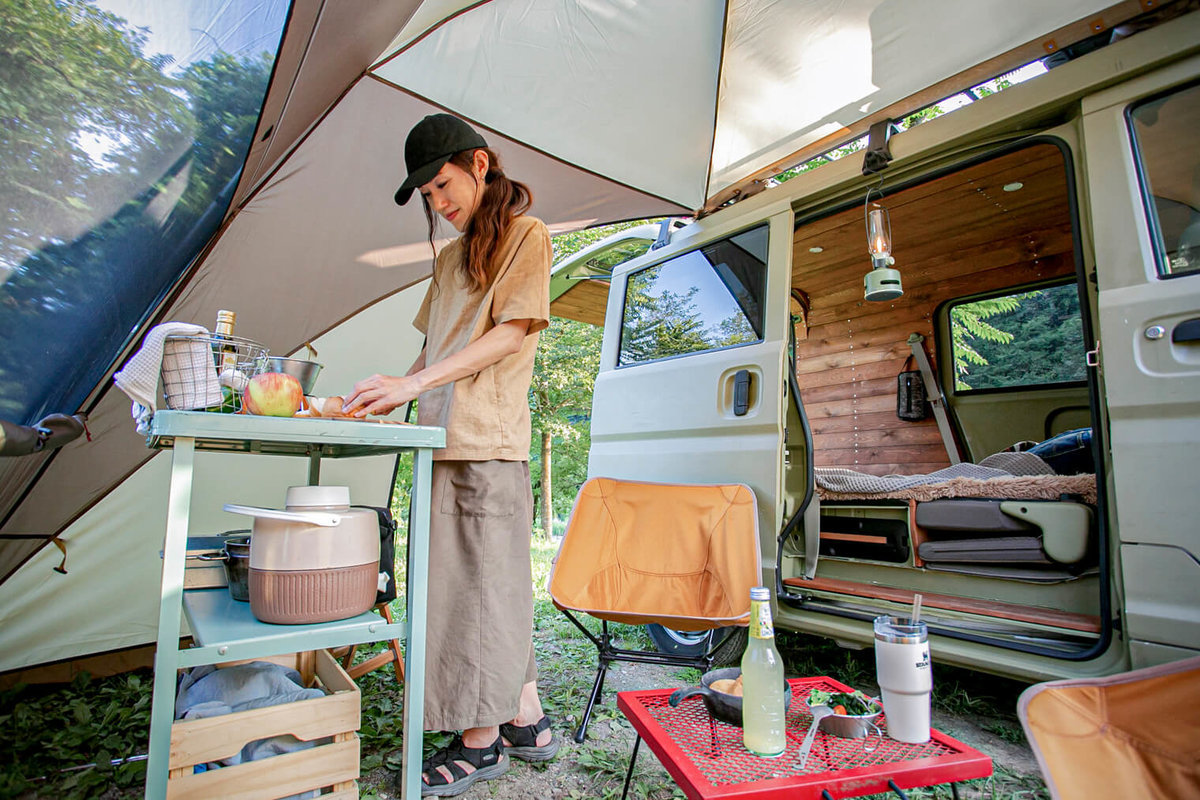４０ 　レトロなカスタムカー。キャンプコーディネーターの三沢真実さん。カーサイドシェルターの中で料理をしている。おしゃれなインテリア