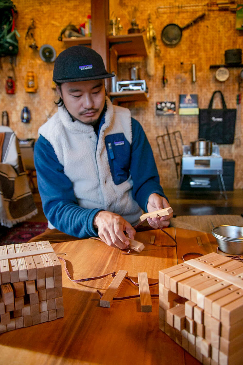 キャンプ民泊「NONIWA（ノニワ）」のリビングルームで木工製品の説明をする野あそび夫婦のアオさん