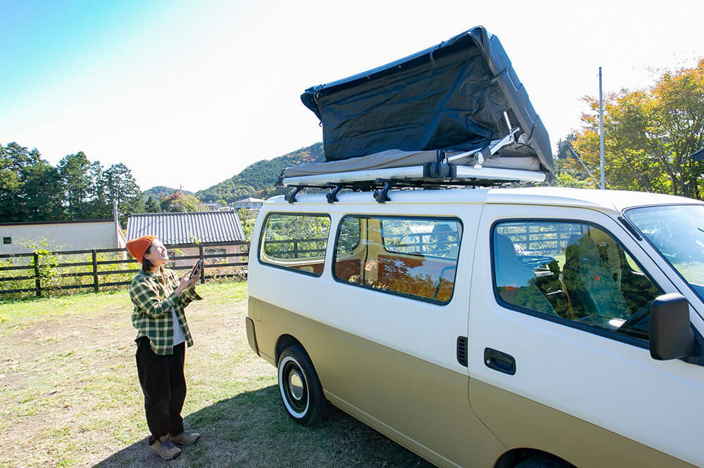 野あそび夫婦のバンライフ車、ルーフトップテントをスマホのアプリで開いているエリーさん