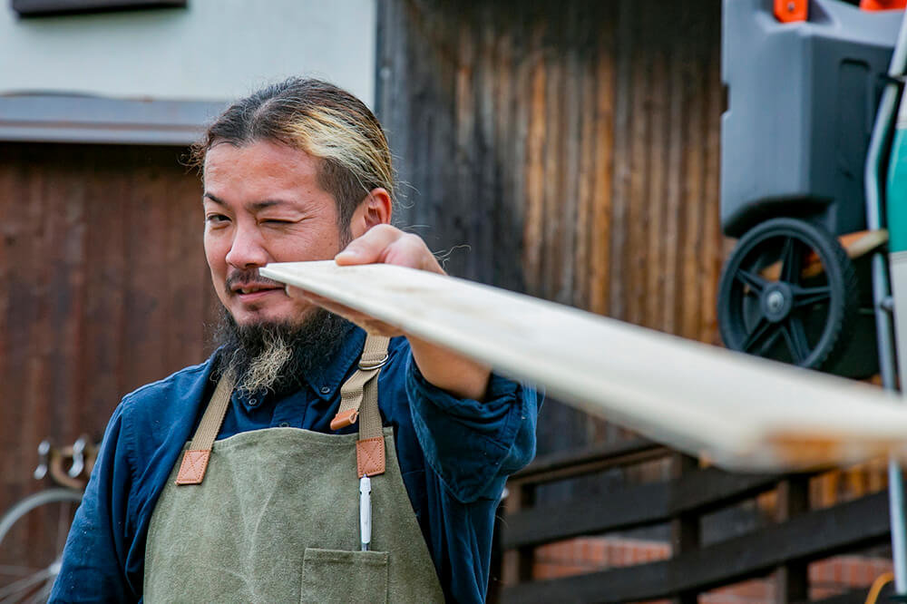 緩やかなカーブをつけた板を、片目をつぶって見ている鈴木さん