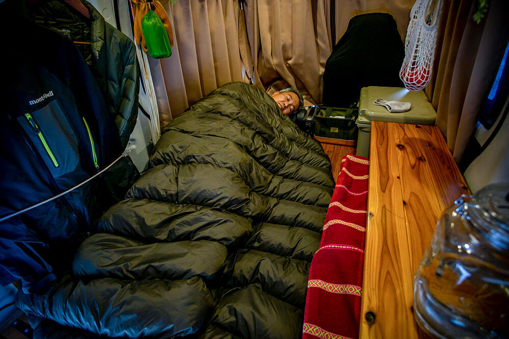 車内のカーテンを閉め、ハイランダーの封筒型ダウンシュラフに入り、渡辺さんが寝ているところ