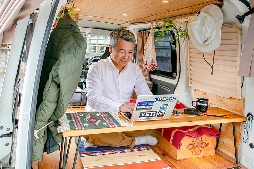 サイドテーブルをリア側に横置きして、外を眺めながら仕事をする渡辺圭史さん