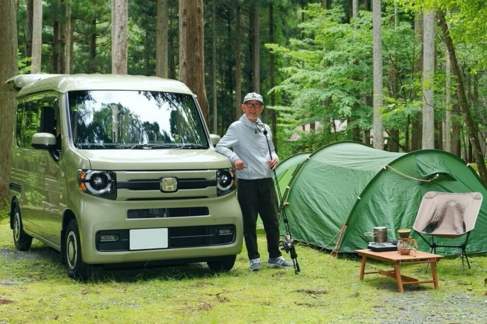 森の中のキャンプ場にて、N-VAN(エヌバン)の横で釣り竿を持って立つ男性