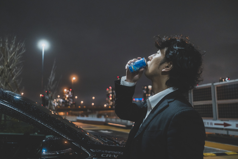 夜景を眺めながら缶コーヒーを飲む男性