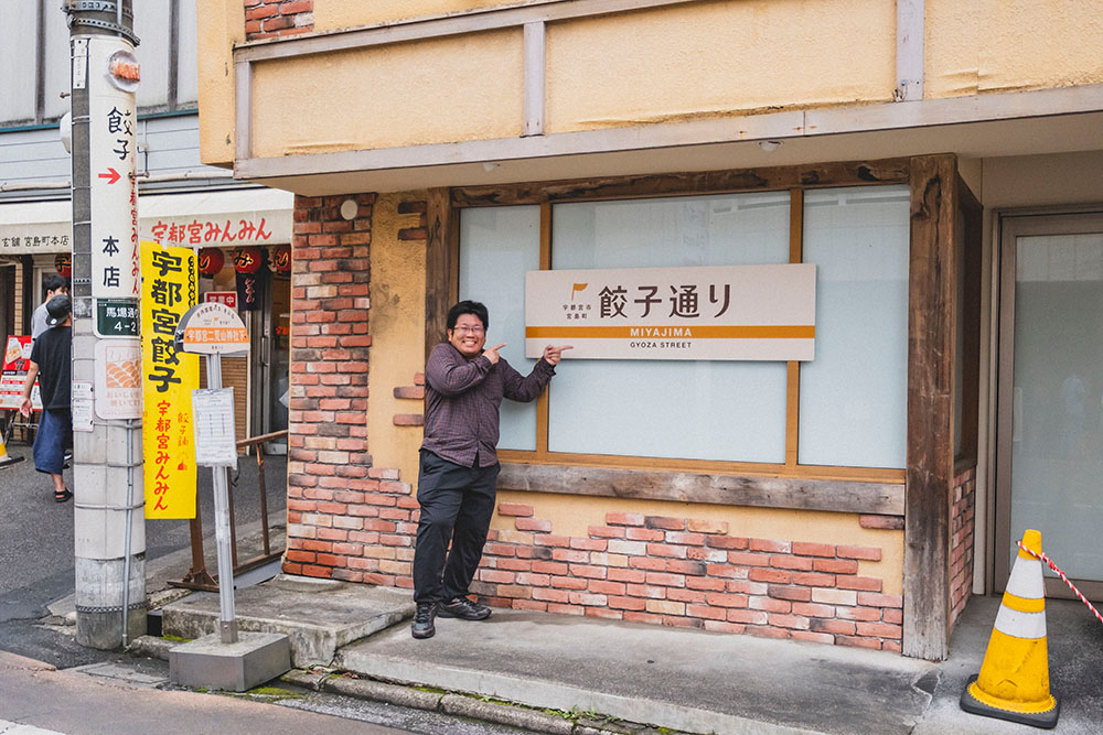 餃子通りの看板で記念写真を撮る少年Bさん