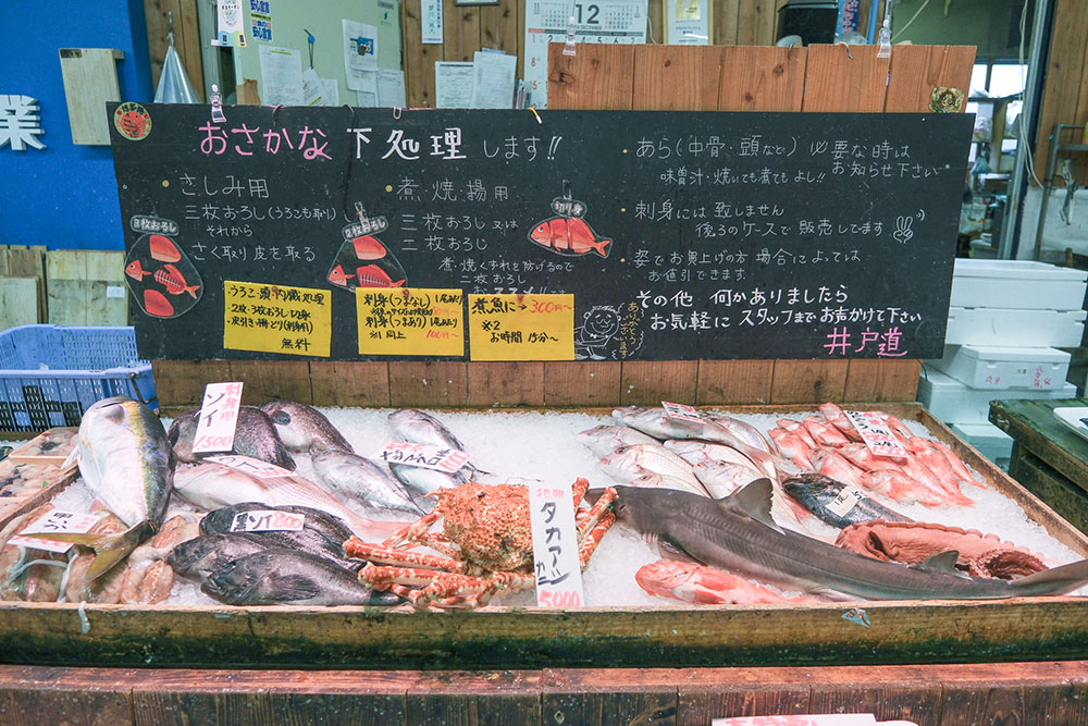 「おさかな下処理します」の看板の下にさまざまな魚が並んでいる