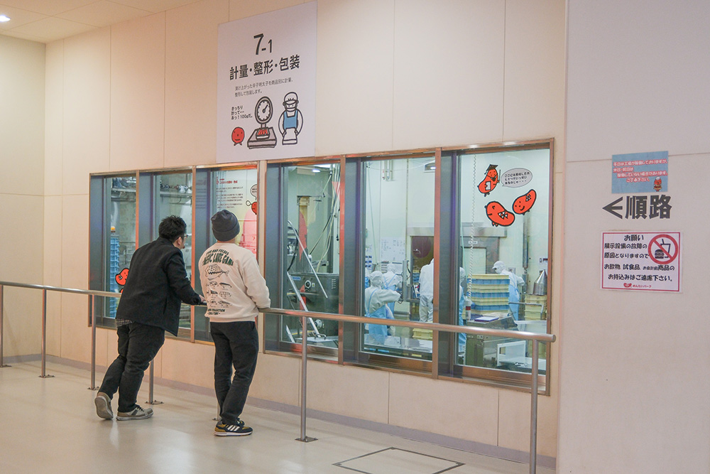 工場見学の大きな窓から工場を眺める２人