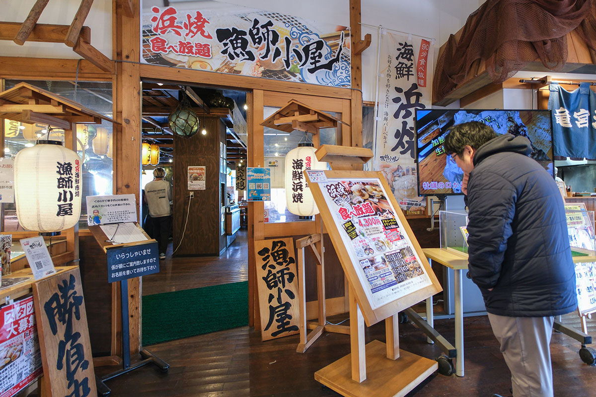 龍宮海鮮市場の中にある浜焼き食べ放題店の前で考える少年B
