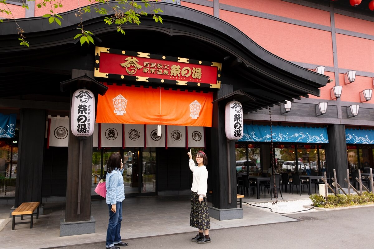 「西武秩父駅前温泉 祭の湯」の入り口に立つ開運したい女性たち