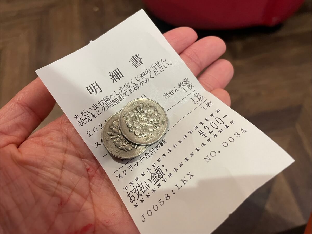 当選した宝くじを引き換えた現金200円と明細書を手に持っている