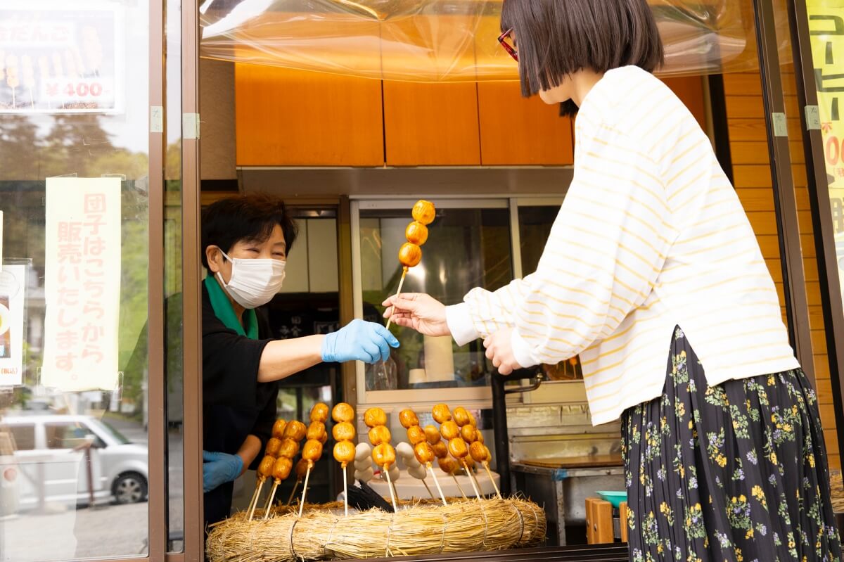 売店で焼きたての黄金だんごを受け取るツマミ具依さん