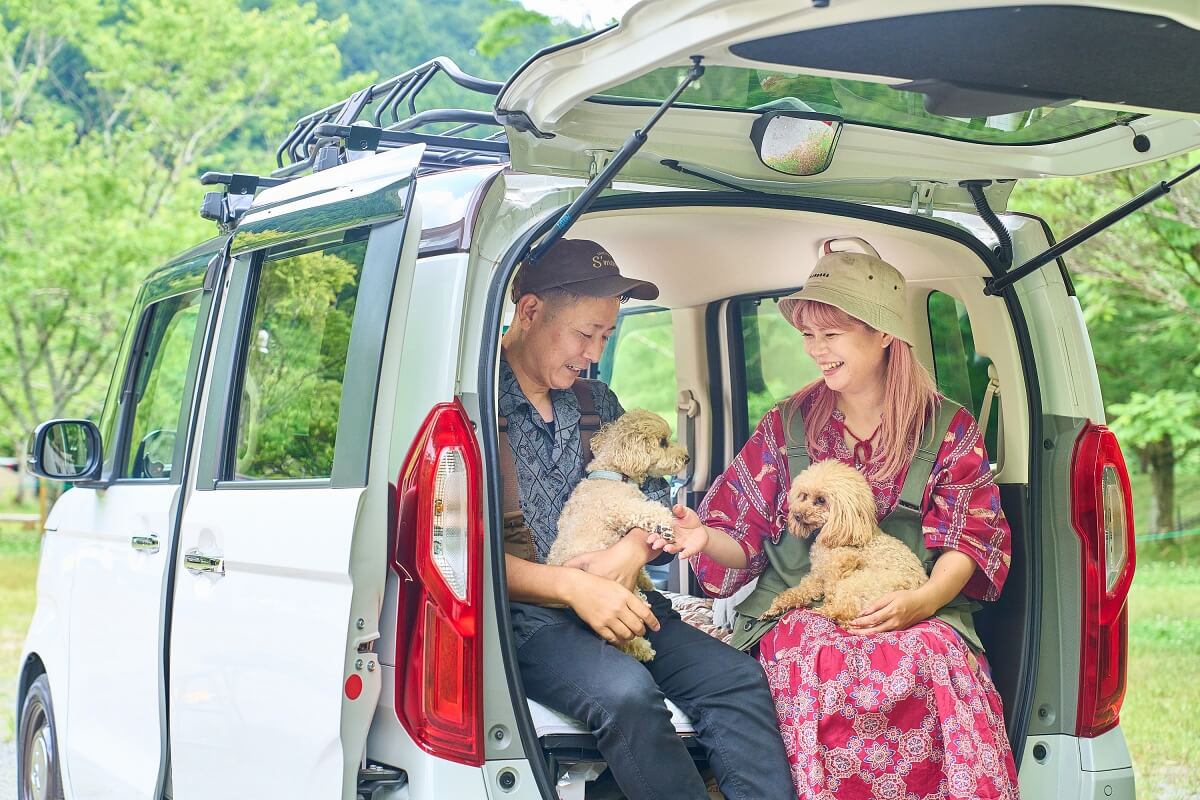 N-BOXのベッドに座り、ペットのトイプードルを膝に乗せて楽しそうに笑っている、さいとう夫婦