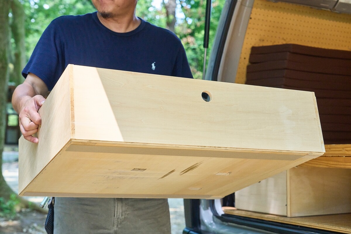 三菱デリカを車中泊カスタム。中古のデリカをキャンピングカーに改造。木製の引き出しを手に持っている宮﨑秀仁さん