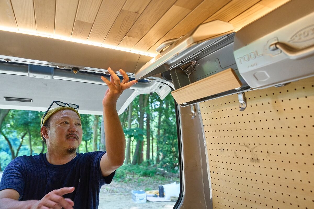 三菱デリカを車中泊カスタム。中古のデリカをキャンピングカーに改造。デリカバンの車内、 ツールボックス(工具箱)の吊り戸棚を開けている宮﨑秀仁さん