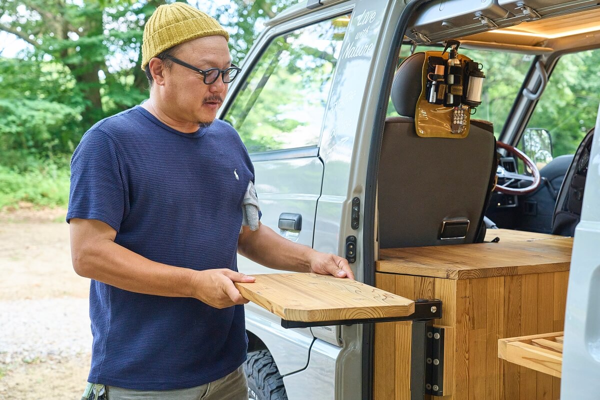 三菱デリカを車中泊カスタム。中古のデリカをキャンピングカーに改造。デリカバンの車内に設置した可動式のテーブルを動かしている宮﨑秀仁さん