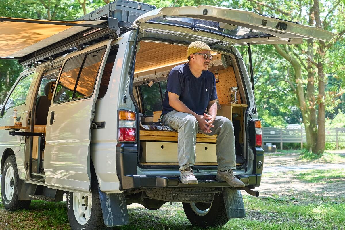 三菱デリカを車中泊カスタム。中古のデリカをキャンピングカーに改造。車中泊カスタムをしたデリカバンのベッドの上に座っている宮﨑秀仁さん