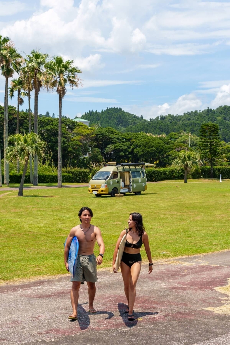 バンライフで日本一周中の【ちゃんじろー夫婦】、サーフボードを手に持ち、サーフィンをするために海に向かって歩いているところ