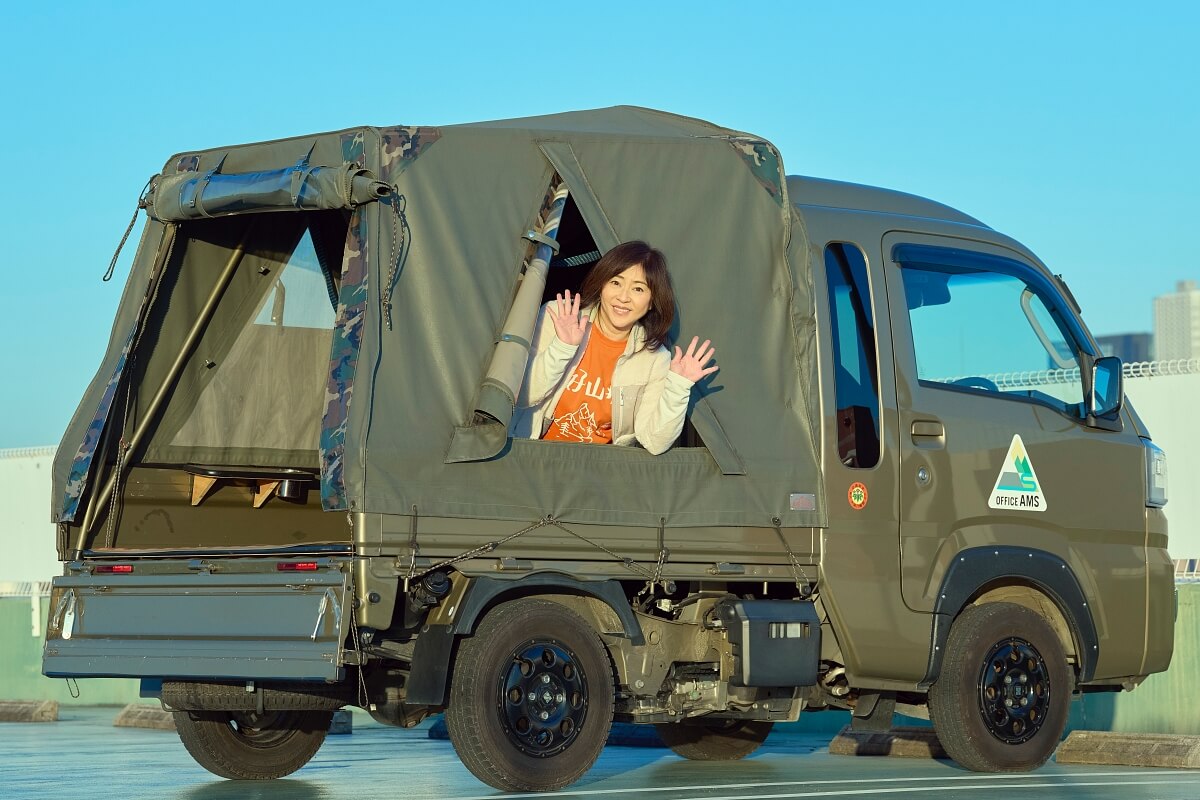 バグトラ荷台のテントの三角窓から顔を出す松本明子さん
