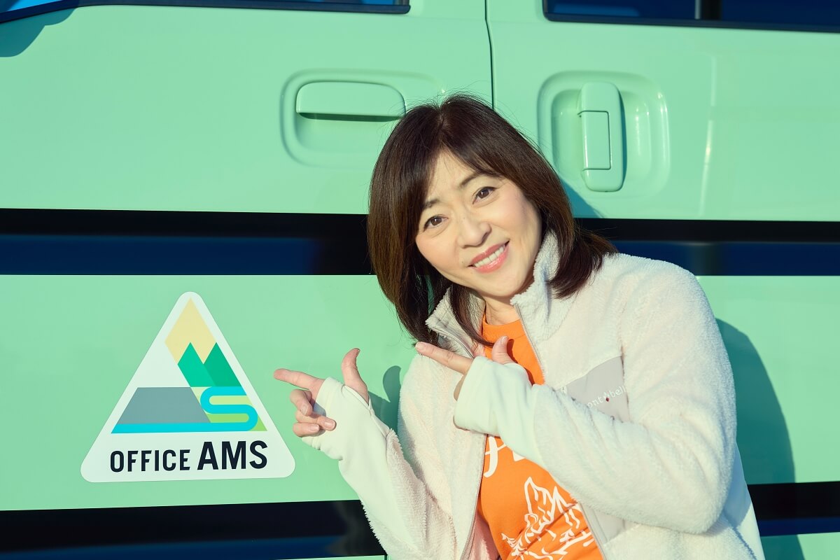 車の貼ったオフィスアムズのステッカーを指差す松本明子さん