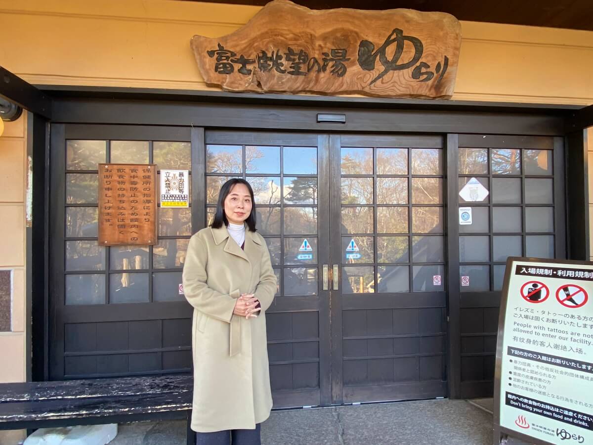  日帰り天然温泉「富士眺望の湯　ゆらり」の看板の前に立つ辛酸なめ子さん